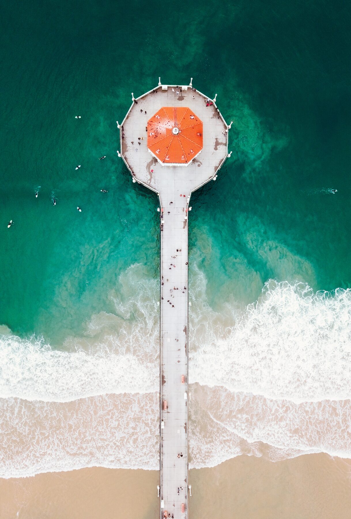 Aerial view of a pier running out over green water, ending in a round orange roof.
