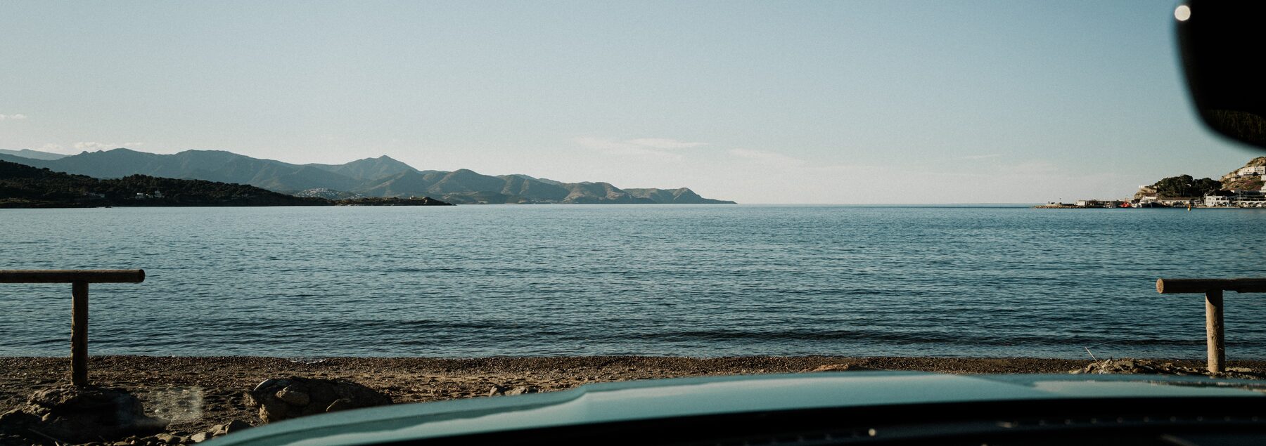 A calm bay and distant hills seen over the bonnet of a parked car.