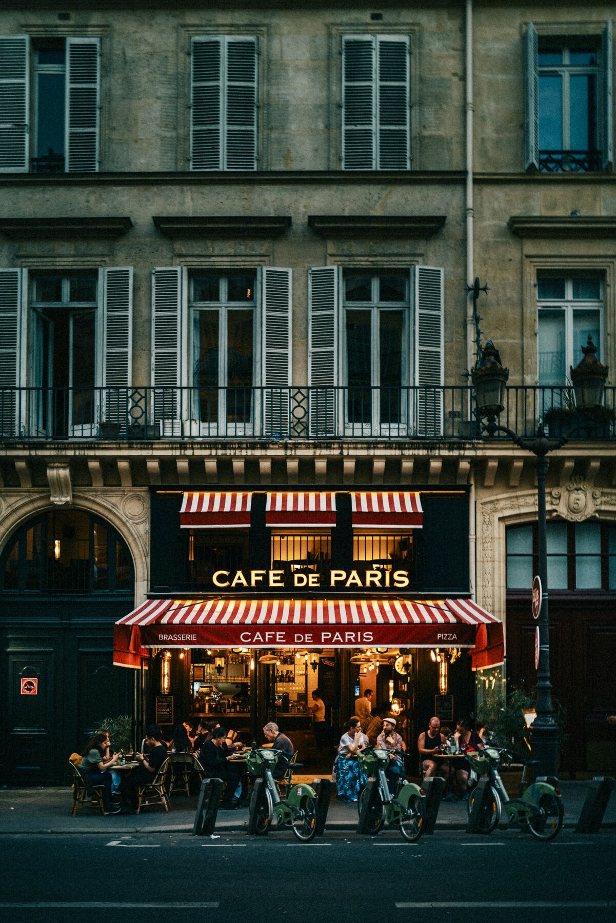 A stone apartment building above the red striped awning of a busy café.